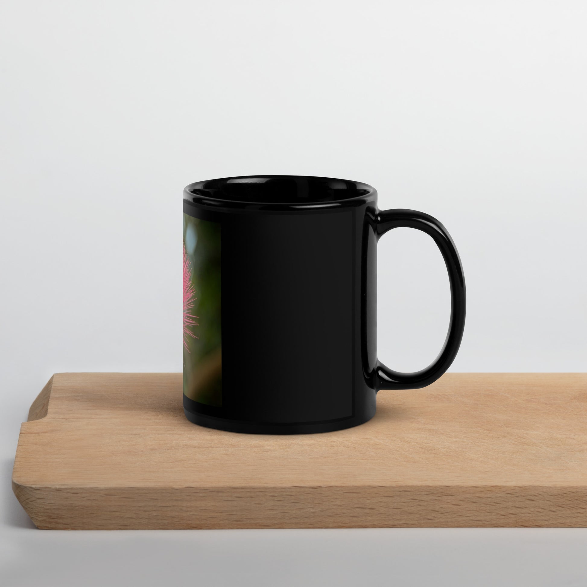 Black glossy ceramic mug with red powder-puff flower design from Calgary Zoo, Alberta, on a wooden board.