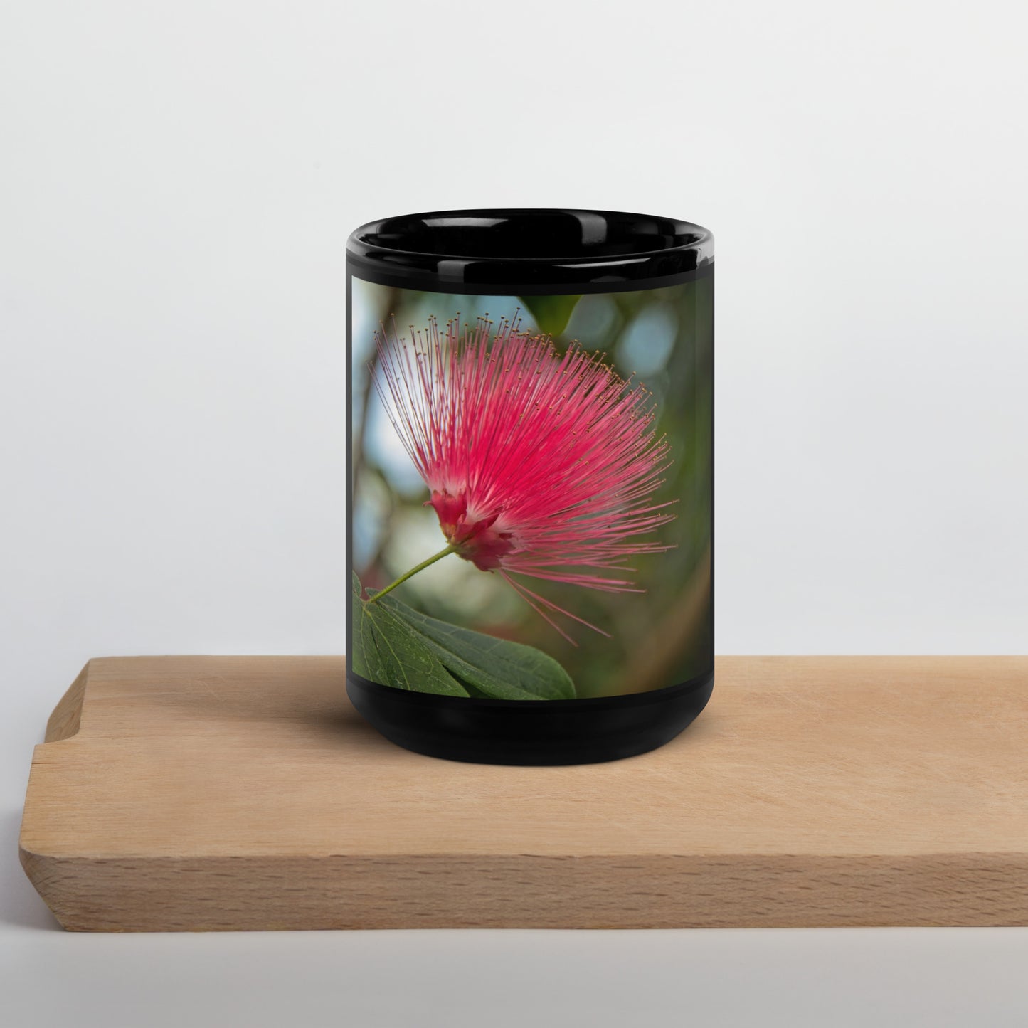 Black glossy ceramic mug with Calgary Zoo Alberta red powder-puff flower photo on green leaves.